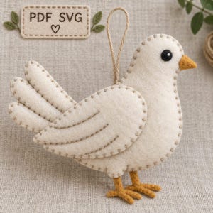 Peut inclure: Un ornement d'oiseau en feutrine crème avec des coutures apparentes marron sur les bords, un petit bec jaune moutarde et des pattes assorties. Un œil noir circulaire est présent, et une fine boucle de ficelle est fixée au sommet. Une étiquette rectangulaire au-dessus indique PDF SVG avec un symbole de cœur.