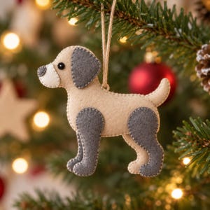 May include: A felt dog ornament in beige and gray with a black bead eye and a jute twine loop for hanging. The dog features a beige body, gray ears, and gray legs, with visible stitching along the edges of the felt pieces to secure the layers.