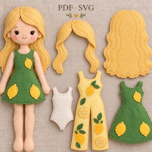 Puede incluir: Una muñeca de fieltro con cabello rubio que viste un vestido verde con motivos de limones amarillos. Se incluyen una pieza de cabello rubio separada, un mono amarillo con estampado de limones, un leotardo blanco y otro vestido verde.