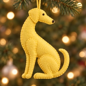 May include: A yellow felt dog ornament featuring a stitched edge design, a small black circular eye, and a black nose. The dog is depicted in a seated position with its tail curved upward, suspended by a thin yellow string loop at the top.