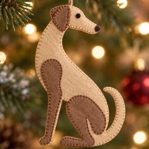 May include: A felt dog ornament in beige and brown with visible stitched edges. The dog is in a seated position with a long neck, a small dark eye, and a dark nose. A thin twine loop is attached to the top of the head for hanging purposes.