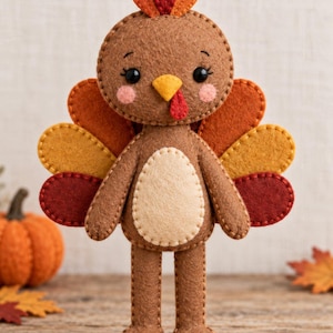 May include: A felt turkey ornament featuring a brown body with a cream-colored belly, a yellow beak, and a red wattle. The tail feathers are layered in shades of orange, yellow, and dark red. The head has black eyes and pink cheeks.