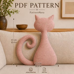 Peut inclure: Un patron PDF pour un coussin en forme de chat, intitulé PatternNora. Le chat en tissu rose présente des yeux fermés brodés. Les dimensions indiquées sont de 53 cm de hauteur et 42 cm de largeur. Des icônes indiquent l'impression à domicile et le format PDF.