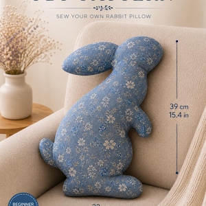 Può includere: Un modello PDF per un cuscino a forma di coniglio con il testo PDF PATTERN SEW YOUR OWN RABBIT PILLOW. Il cuscino è realizzato in tessuto blu con una stampa floreale bianca. Le dimensioni sono 39 cm di altezza e 32 cm di larghezza.