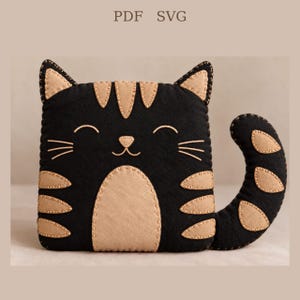 Pode incluir: Uma pelúcia de gato quadrada em feltro preto com detalhes em feltro bege nas orelhas, testa, peito e cauda. O gato apresenta olhos fechados bordados, um nariz pequeno, bigodes e listras. O texto PDF SVG é visível na parte superior.