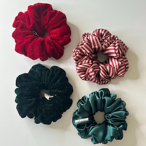 May include: Four scrunchies in various colors and textures. One is red velvet, another red and white striped, a third is dark green velvet, and the last is a dark green satin. Each scrunchie is circular and gathered.