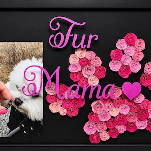 May include: A framed black artwork with the words "Fur Mama" in pink script. The artwork includes a photo of a white dog, paper roses, and a pink heart. The roses are in shades of pink.