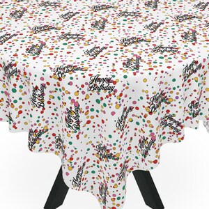 May include: A round white tablecloth with a colorful confetti pattern and the words "Happy Birthday" in black script. The tablecloth is draped over a black table with three legs. The confetti includes red, yellow, green, and purple dots.