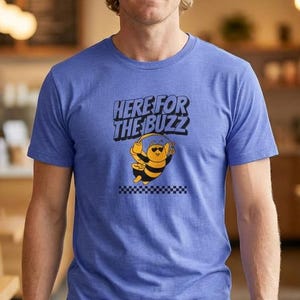 May include: A blue t-shirt with the text "HERE FOR THE BUZZ" and a cartoon bee wearing sunglasses and giving a thumbs up. The bee is on a checkered pattern. The person is wearing blue jeans.