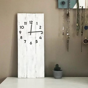 May include: White wooden clock with black numbers and hands. The clock is hanging on a wall with a light brown background.