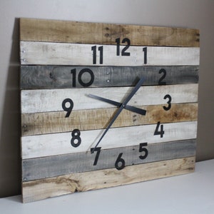 May include: A large, rustic clock made from reclaimed wood planks. The clock face is painted white with black numbers and hands. The clock is hanging on a wall.