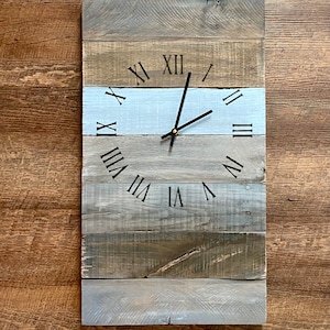 May include: A rustic wooden clock with Roman numeral markings on a light blue, gray, and brown background.