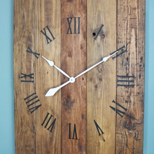 May include: A rustic wooden clock with Roman numeral markings and white hands. The clock is made from reclaimed wood planks and has a distressed finish.