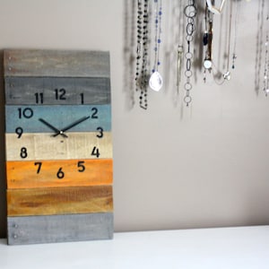 May include: A colorful wooden clock with black numbers and hands. The clock is made of reclaimed wood and has a rustic look.