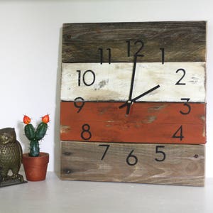 May include: A rustic wooden clock with black numbers and hands. The clock face is made of three horizontal planks of wood painted white, orange, and brown.