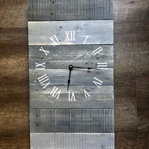 May include: A rustic wooden clock with Roman numeral markings on a gray and white painted background.
