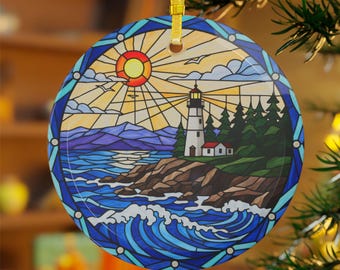 Könnte beinhalten: Runder Keramikschmuck mit einem Buntglasdesign, das einen Leuchtturm an einer felsigen Küste zeigt. Der Schmuck hat einen blauen Rand und ein goldenes Band zum Aufhängen. Die Szene umfasst Sonne, Vögel und Meereswellen.
