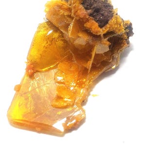 Könnte beinhalten: Nahaufnahme einer Mineralprobe mit einer Mischung aus Farben. Die Probe hat eine durchscheinende, bernsteinfarbene kristalline Struktur mit einem dunkelbraunen, strukturierten Bereich. Das Mineral ist vor einem weißen Hintergrund platziert.