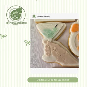 Peut inclure: Un biscuit en forme de main tenant un verre à martini avec du liquide vert et des olives, avec des détails en glaçage blanc. L'image inclut le texte 3D PRESS AND BAKE et Digital STL File for 3D printer, indiquant un fichier de conception numérique.