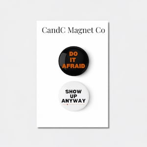 May include: Two round magnets with motivational phrases. The top magnet is black with orange text that reads "DO IT AFRAID." The bottom magnet is white with black text that reads "SHOW UP ANYWAY."