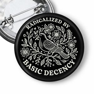 May include: Black button pin with a white illustration of a bird perched on a floral branch. The text "RADICALIZED BY BASIC DECENCY" is in a circular pattern around the bird. A silver pin back is visible.