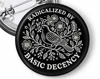 Puede incluir: Pin negro con una ilustración blanca de un pájaro posado en una rama floral. El texto "RADICALIZED BY BASIC DECENCY" está en un patrón circular. Se ve un alfiler plateado en la parte posterior.