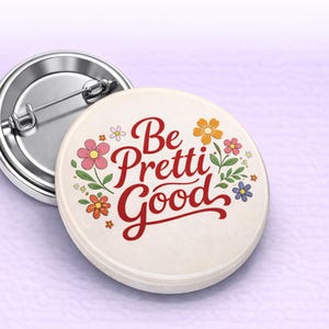 May include: A round button with the phrase "Be Pretti Good" in red script, surrounded by colorful floral illustrations. The button has a cream-colored background and a silver metal pin backing.