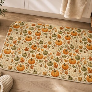 Peut inclure: Un tapis de sol rectangulaire orné d'un motif répétitif de citrouilles orange, blanches et vertes entremêlées de feuilles d'automne brunes, orange et vertes sur un fond crème, avec des coins arrondis et un bord en tissu fini.