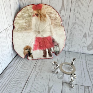 May include: A decorative, round coaster with a winter scene featuring a person in a red coat and hat, walking with a dog. A silver metal stand with ornate legs is also present.
