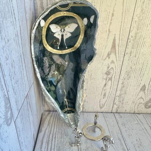May include: A decorative, silver-edged tray with a dark, patterned interior featuring a white moth within a gold circle. The tray has a silver metal stand with three decorative feet.