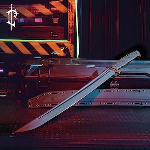 May include: A large, silver blade with a textured handle and orange accents. The blade is angled and appears sharp. The handle has a gray and black pattern. The background is a dark, industrial setting with a logo in the upper left corner.