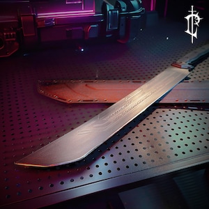 May include: A long, silver blade with etched linear designs, possibly a sword or knife. The blade has a curved edge and a red accent near the handle. It rests on a perforated metal surface with a matching sheath in the background.