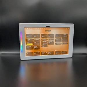 Può includere: Un pannello di controllo per la casa intelligente rettangolare con cornice argentata mostra varie letture ambientali e opzioni di controllo. Lo schermo mostra temperatura, umidità e controlli dell'illuminazione. Una striscia LED colorata corre lungo il lato sinistro della cornice.