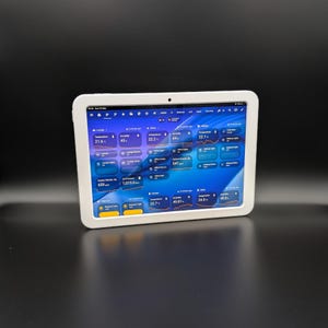 May include: A white tablet displaying a smart home control interface with a black screen. The screen shows temperature, humidity, and light settings. The tablet is in a white frame and rests on a black surface. Measurements are in Celsius.