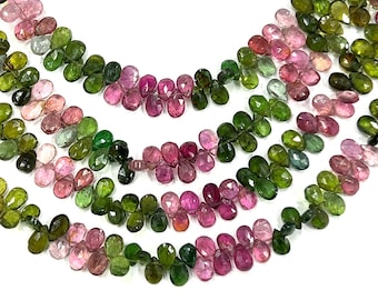 May include: Close-up of strands of multi-colored tourmaline beads. The beads are teardrop-shaped and range in color from deep green to pink and peach. The beads are strung together, creating a layered effect against a white background.