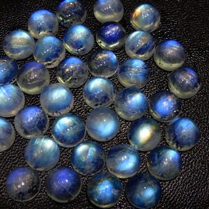 K&ouml;nnte beinhalten: Eine Sammlung runder, polierter Mondstein-Cabochons. Die Steine zeigen eine Mischung aus blauen und wei&szlig;en Farben mit einem durchscheinenden Aussehen. Die Edelsteine sind eng aneinander angeordnet und zeigen ihre nat&uuml;rliche Sch&ouml;nheit und ihr Potenzial f&uuml;r die Schmuckherstellung.