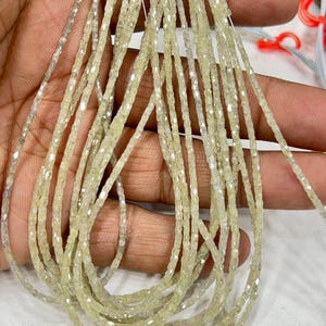 May include: Multiple strands of small, pale yellow-green, square-cut gemstones. The gemstones are strung together, forming several strands. The gemstones are held in a hand. The date and time 2025/11/15 16:34 are visible.