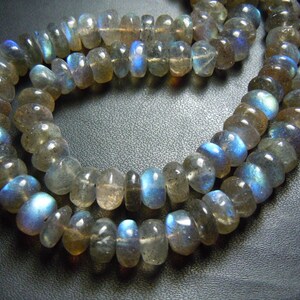 Puede incluir: Primer plano de dos hilos de cuentas de piedra labradorita. Las cuentas son una mezcla de gris, marr&oacute;n y transparente, con destellos de color azul e iridiscente. Las cuentas est&aacute;n ensartadas, creando un collar.