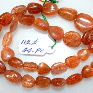 May include: Strands of polished, orange-red sunstone beads. The beads are oval and irregular in shape, with a sparkling, reflective quality. A tag reads "112 t 44-pc".