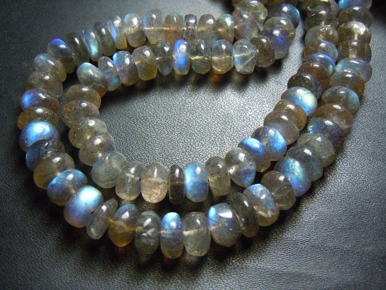 Puede incluir: Primer plano de dos hilos de cuentas de piedra preciosa labradorita. Las cuentas son una mezcla de gris, marr&oacute;n y transparente, con destellos azules iridiscentes. Las cuentas est&aacute;n ensartadas, formando un collar o pulsera.