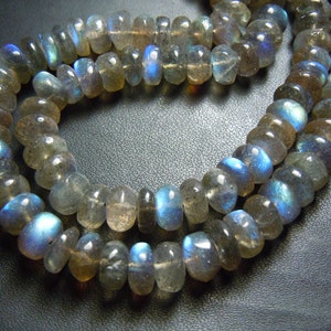 Puede incluir: Primer plano de dos hilos de cuentas de piedra preciosa labradorita. Las cuentas son una mezcla de gris, marr&oacute;n y transparente, con destellos azules iridiscentes. Las cuentas est&aacute;n ensartadas, formando un collar o pulsera.