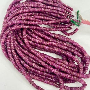 Può includere: Una collezione di fili di perline di pietre preziose di rubino. Le perline sono di un colore magenta intenso e sono tagliate in piccole forme quadrate. I fili sono raggruppati, pronti per la creazione di gioielli.