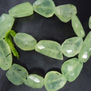 Puede incluir: Un collar de cuentas facetadas de piedra preciosa prehnita verde pálido. Las cuentas tienen una calidad translúcida con inclusiones sutiles y están ensartadas con un hilo verde. Las piedras preciosas tienen forma irregular y están pulidas.