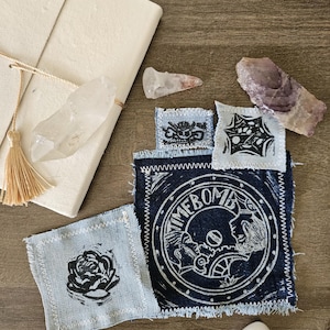 Peut inclure: Plusieurs patchs faits à la main en denim avec divers motifs, dont une rose et le mot « TIMEBOMB », ainsi que des cristaux. Les patchs sont disposés sur une surface en bois. Cristaux incluant quartz et fluorite.
