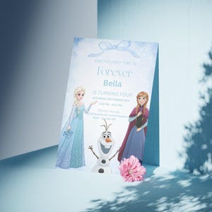 Pode incluir: Um cartão de convite azul claro com o texto "Forever Bella faz quatro anos". O cartão apresenta ilustrações de Elsa, Anna e Olaf do filme Frozen. Uma flor rosa é colocada em frente ao cartão.