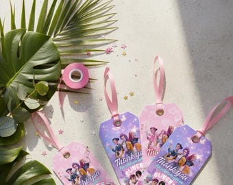 May include: Four pink and purple gift tags with pink ribbons. Each tag features a group of people and the text "Thank you Oliver's". A roll of pink tape and green leaves are in the background.