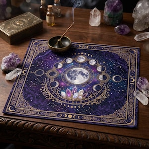 May include: A square purple altar cloth featuring a central full moon surrounded by a lunar cycle, gold celestial patterns, and crystal illustrations. The cloth is decorated with gold borders, zodiac symbols, and constellations on a dark background.