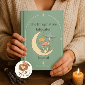 Puede incluir: Un diario verde azulado titulado "The Imaginative Educator" con una ilustración de luna creciente y setas. El diario está sostenido por una persona. Una pegatina con un pájaro y un nido es visible. Una vela encendida y lavanda seca están sobre la mesa.