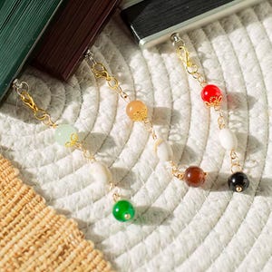 May include: Three gold-toned metal chains attached to rectangular objects, each featuring a series of colorful beads. The beads include shades of light green, white, orange, red, brown, and black, with some beads accented by small gold-toned metal caps.