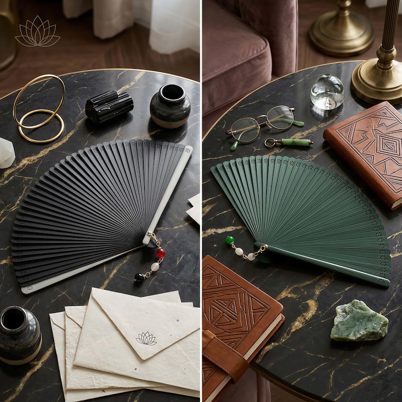 May include: A black folding fan with a beaded tassel and a green folding fan with a beaded tassel. Both fans feature intricate cut-out patterns along the top edge and are displayed alongside stationery, a leather-bound book, and small decorative objects.